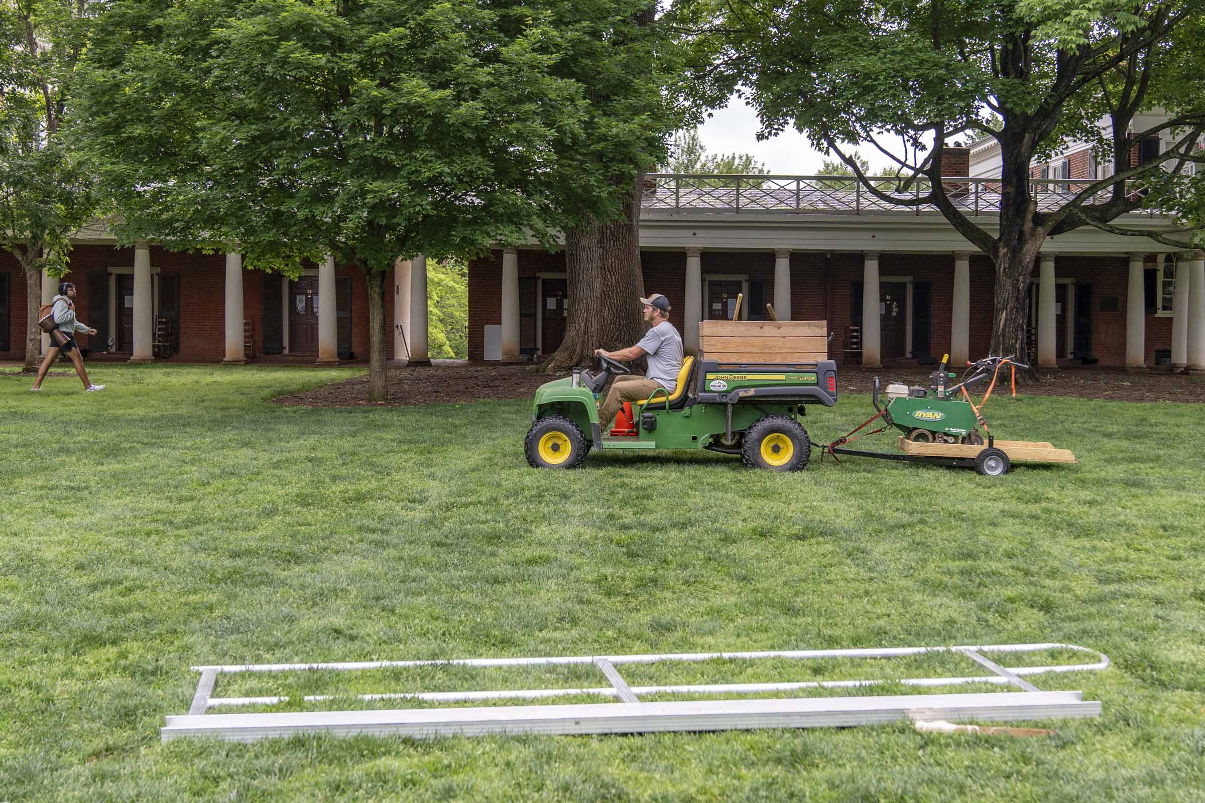 A landscaper drives a John Deer vehicle toting wood to prepare for Final Exercises