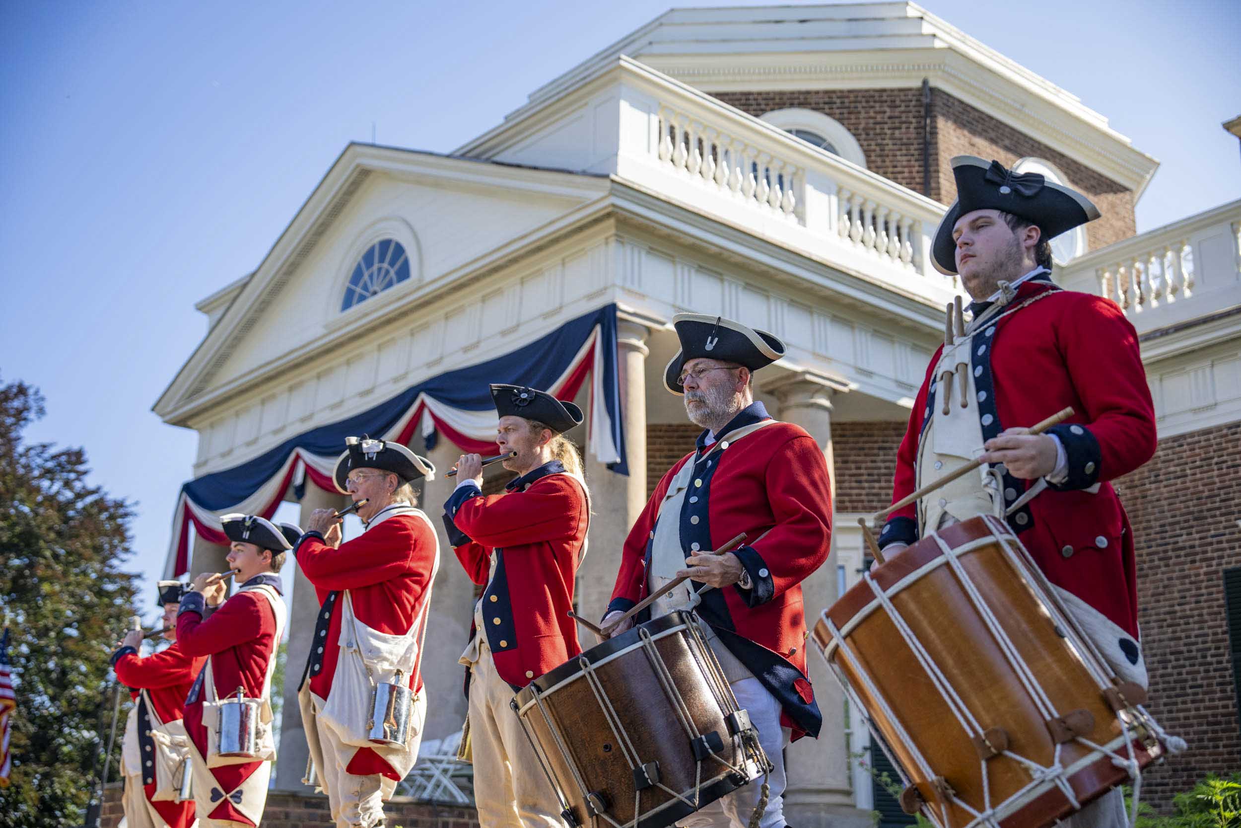 Fife and drummers in colonial red uniforms playing their instruments in front of Monticello.