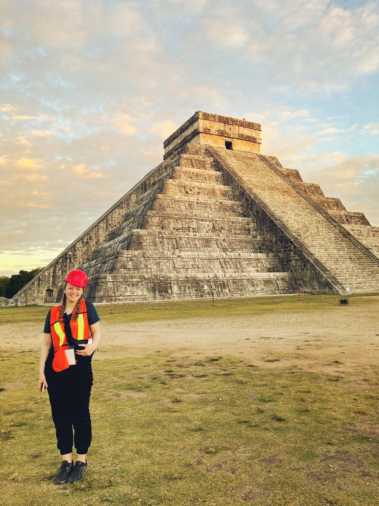 Sydney Roberts in a hard hat and orange vest poses for photo in front of El Castillo