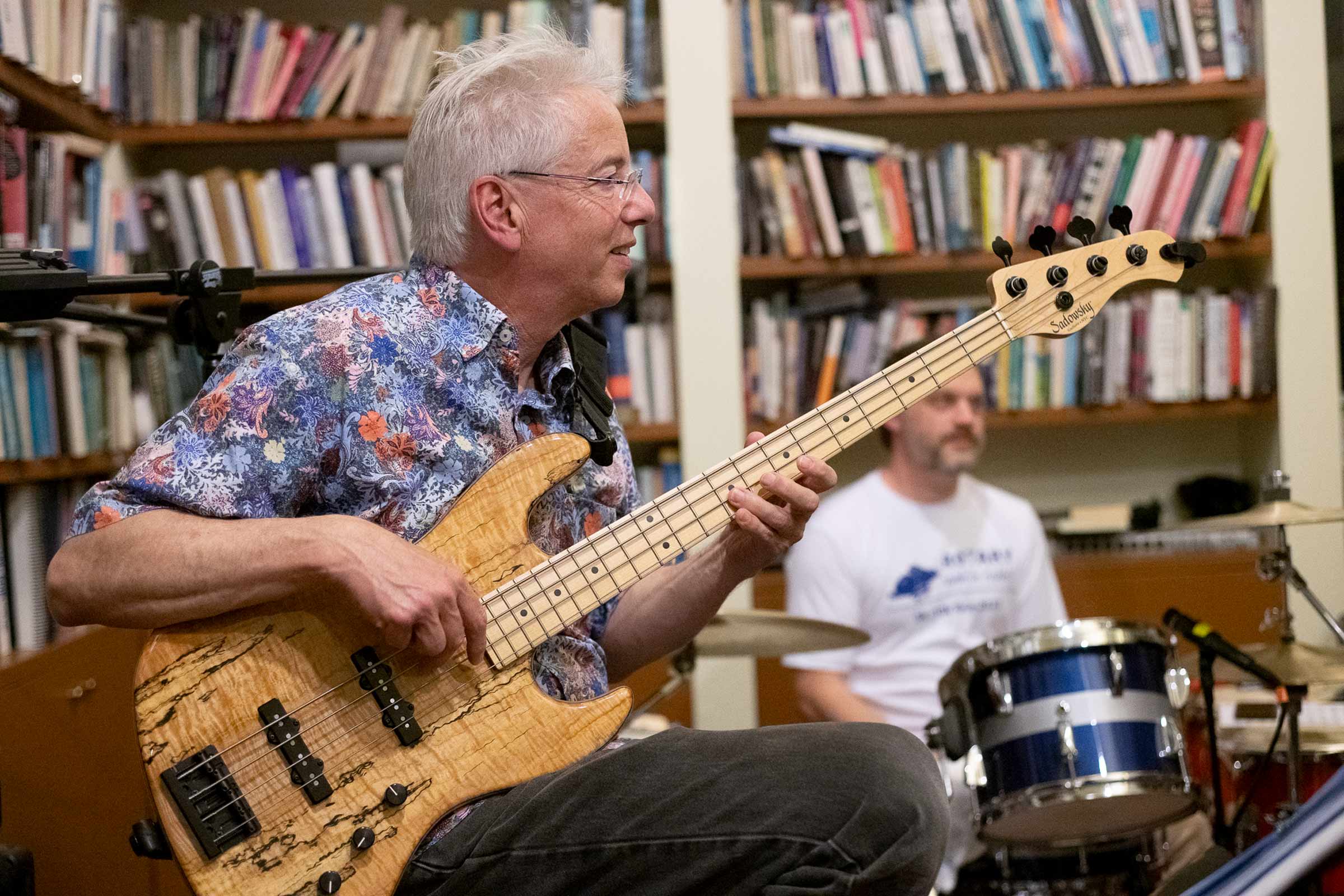 Marc Lipson plays his bass seated in front of expansive bookshelves and smiles