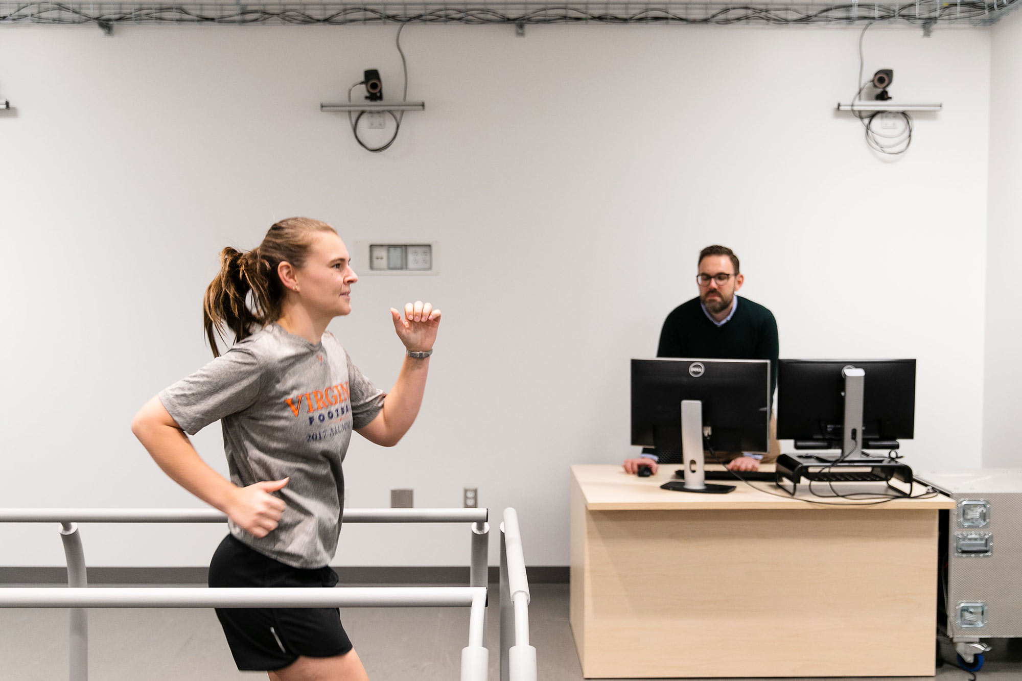 Candid of a participant on a treadmill with Chris Kuenze in the background monitoring the test results on a computer