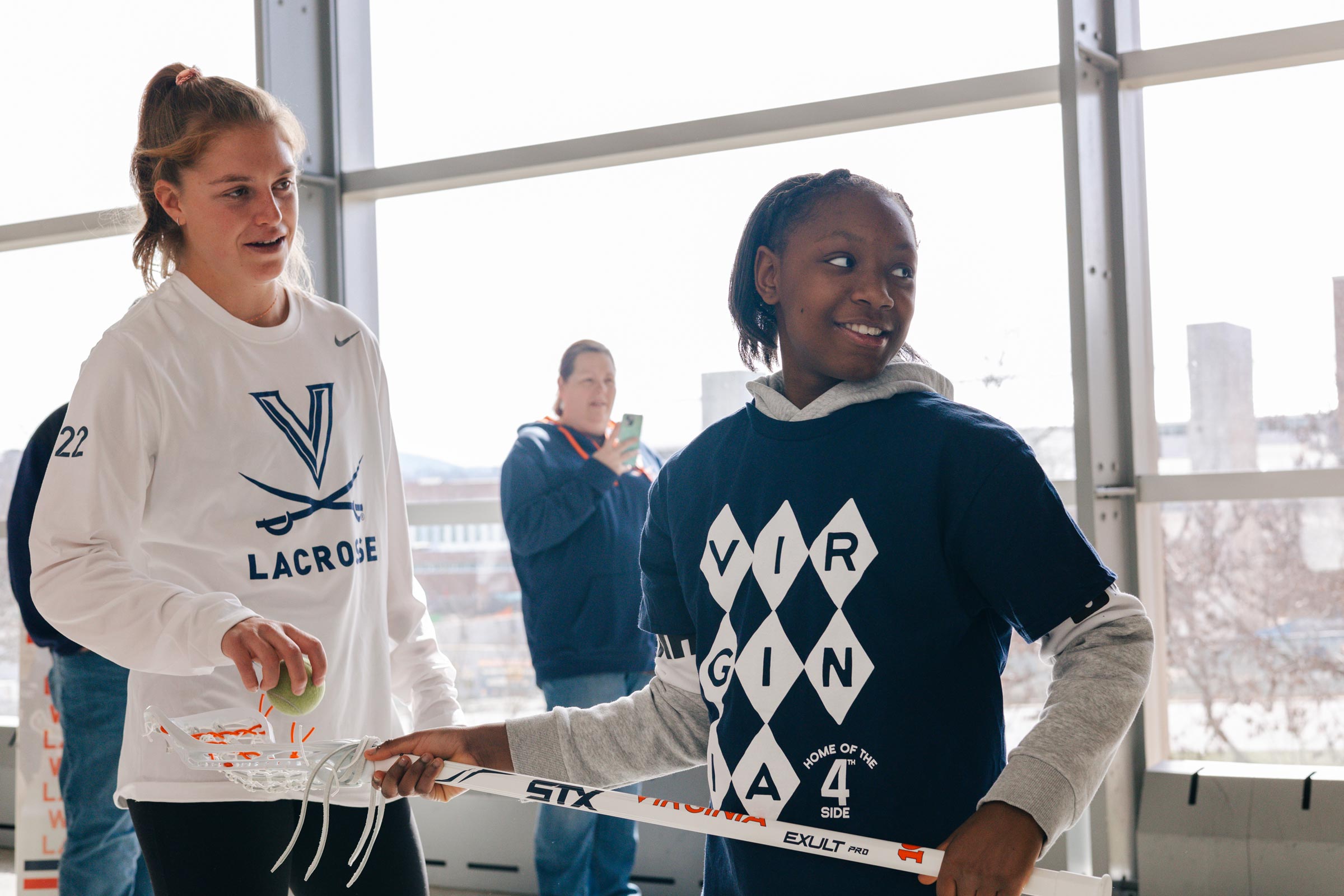 A women's lacrosse member works with a student 