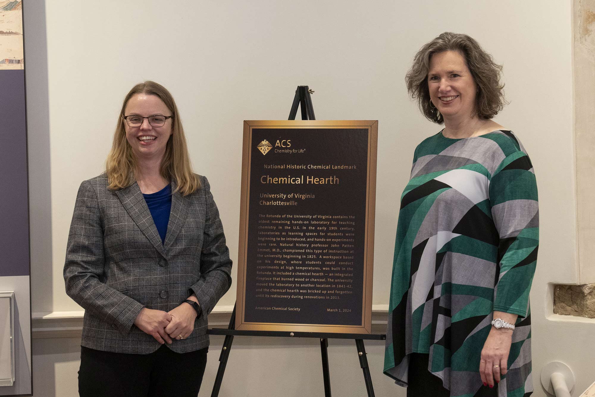 Formal portrait of Jill Venton and Mary K. Carroll standing infront of the historic plaque