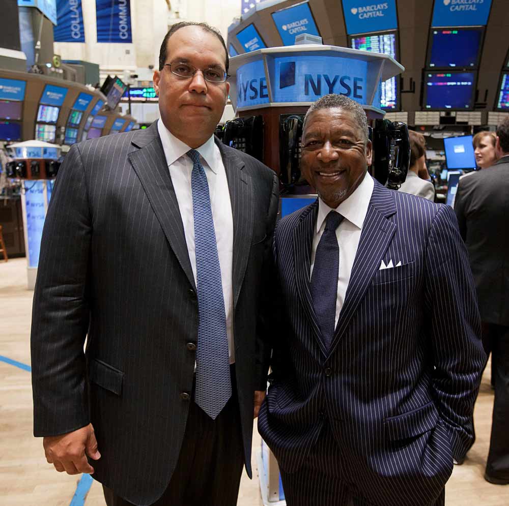Baltimore and Johnson, in suits and ties, pose together inside the New York Stock Exchange