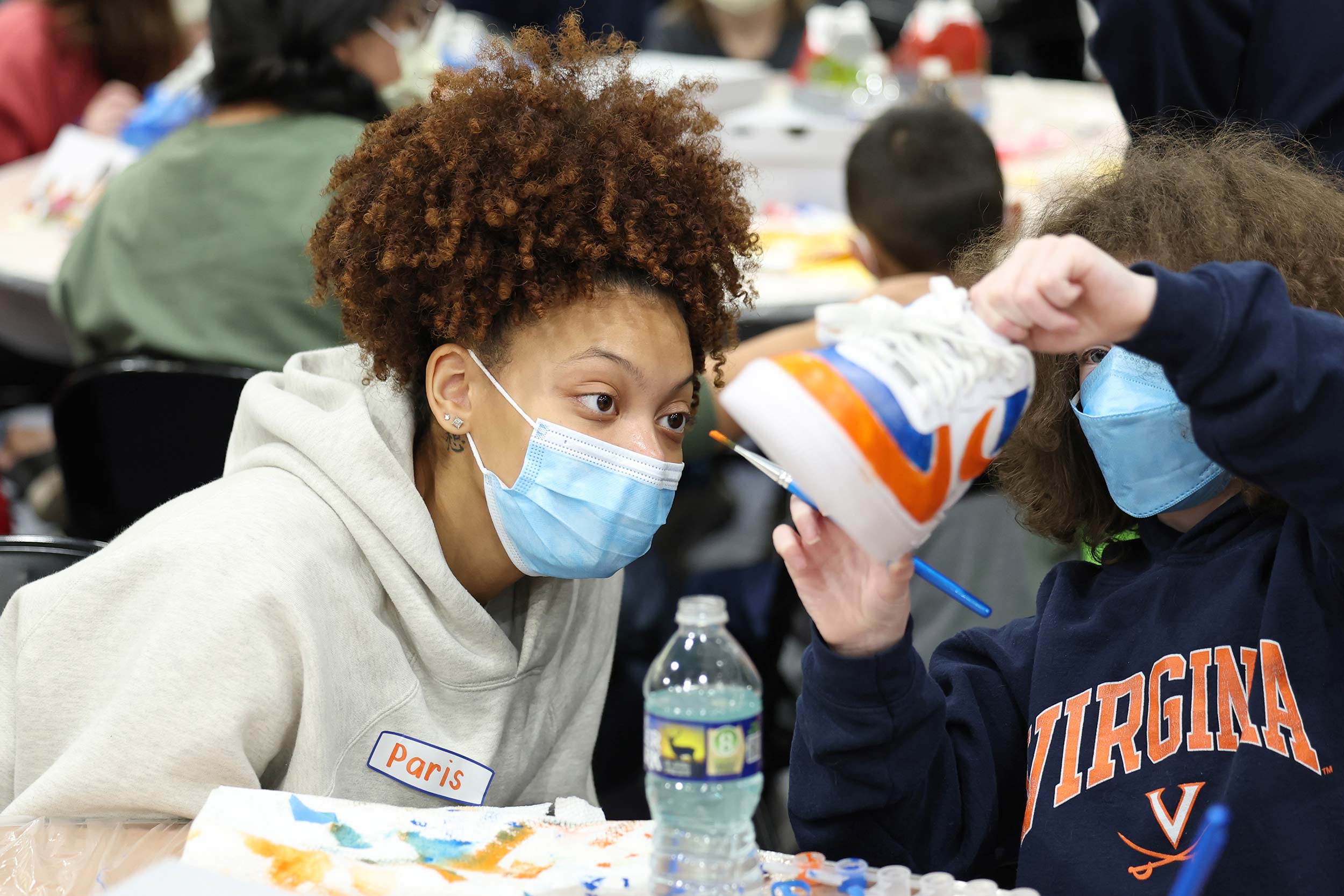 Two students lean in to examine an orange and blue paint job on a shoe