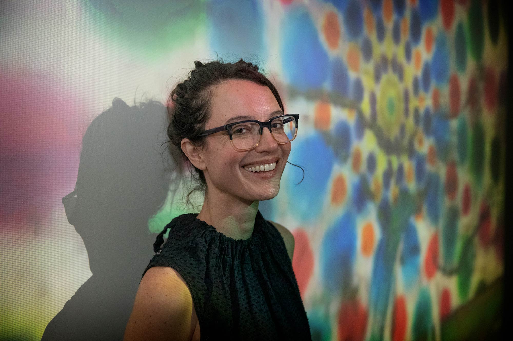 Portrait of Lydia Moyer inside against a backdrop of a digital art light display