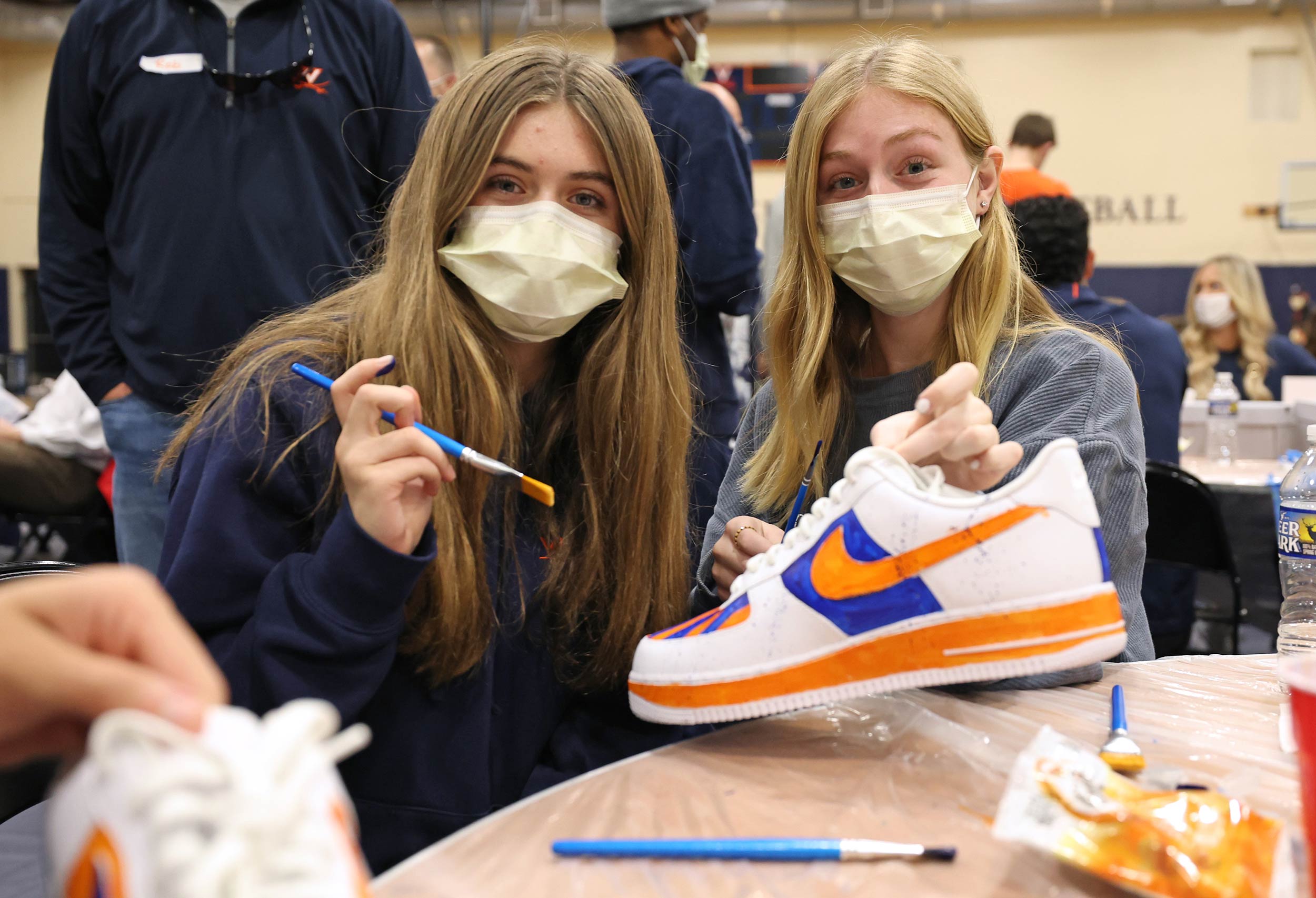 two girls hold up their shoe to show an orange nike swoosh