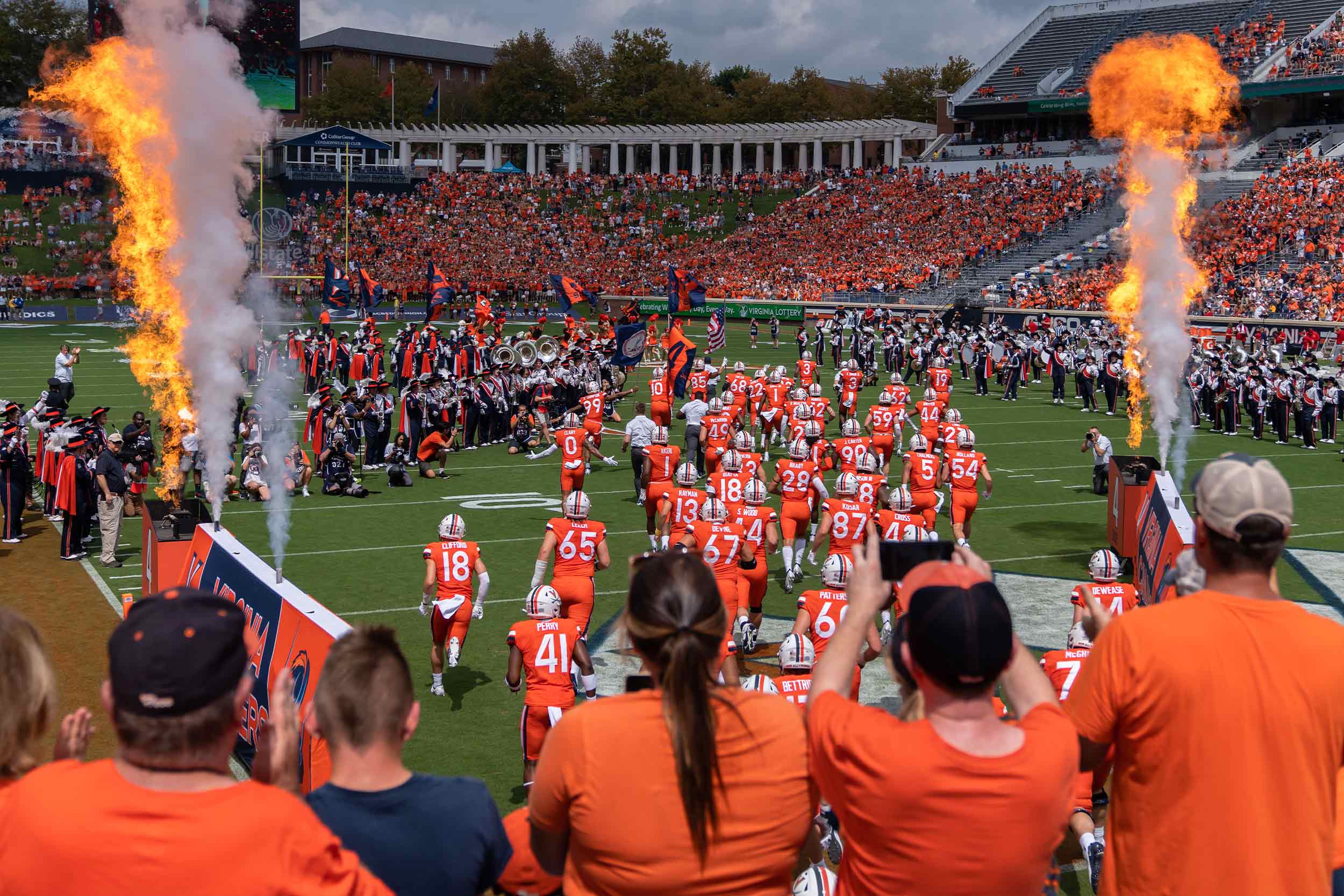 UVA football team running onto the field while flame shoots up into the air while the fans cheer