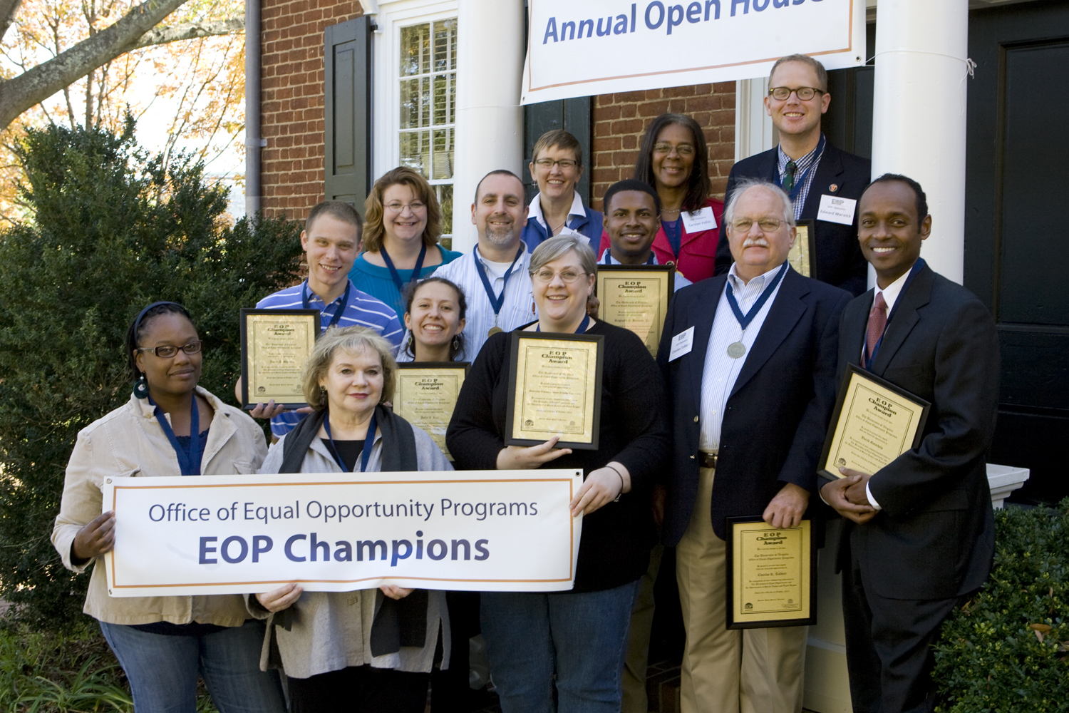 Group photo of people holding framed awards standing on the brick steps of the Equal Opportunity Programs house