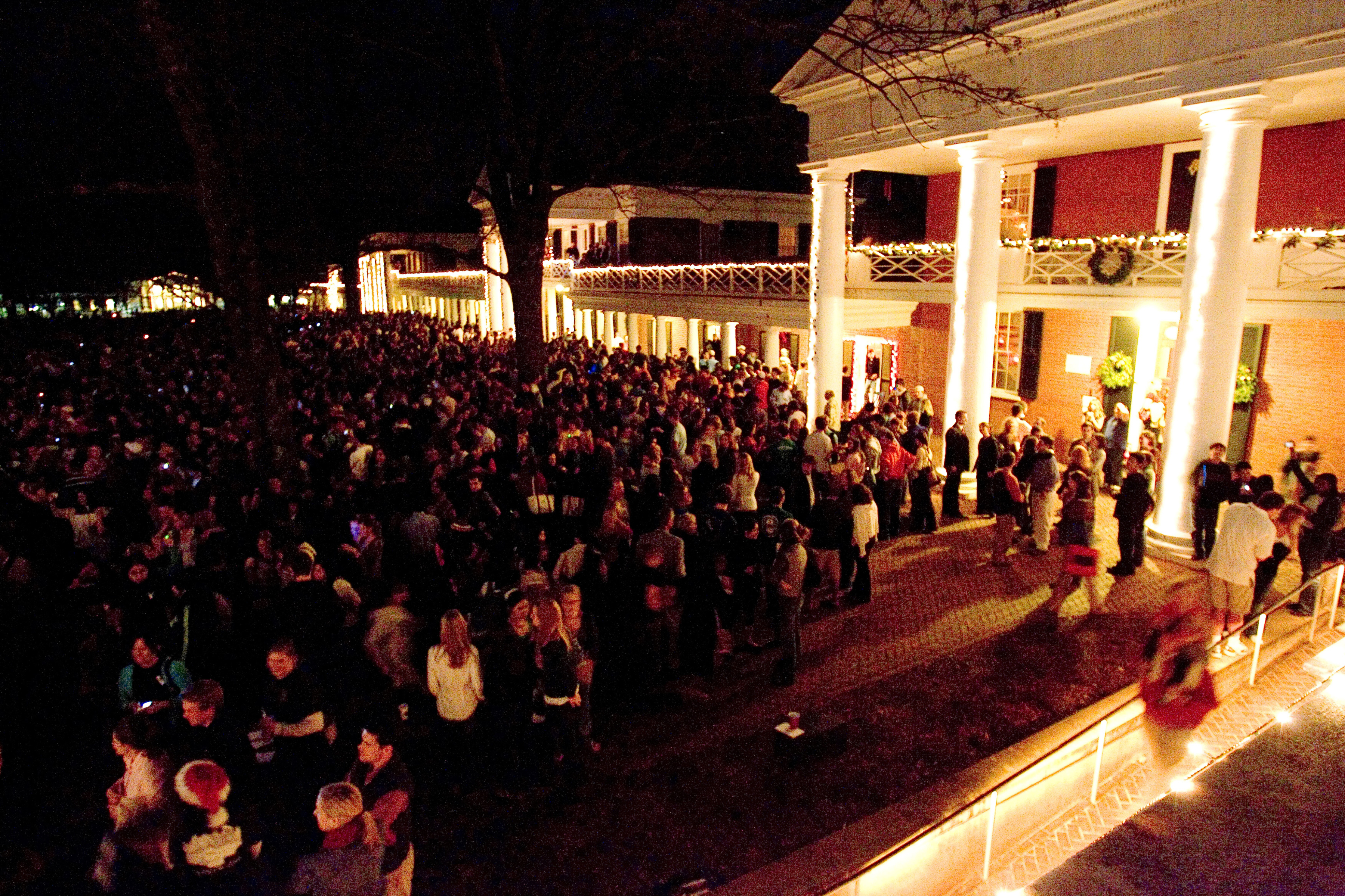 Crowd of people on the lawn at night time with all of the building outlined in white lights