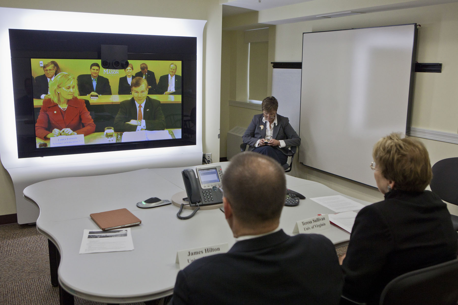 UVA leadership sits at a table and participates in a video conference with other universities