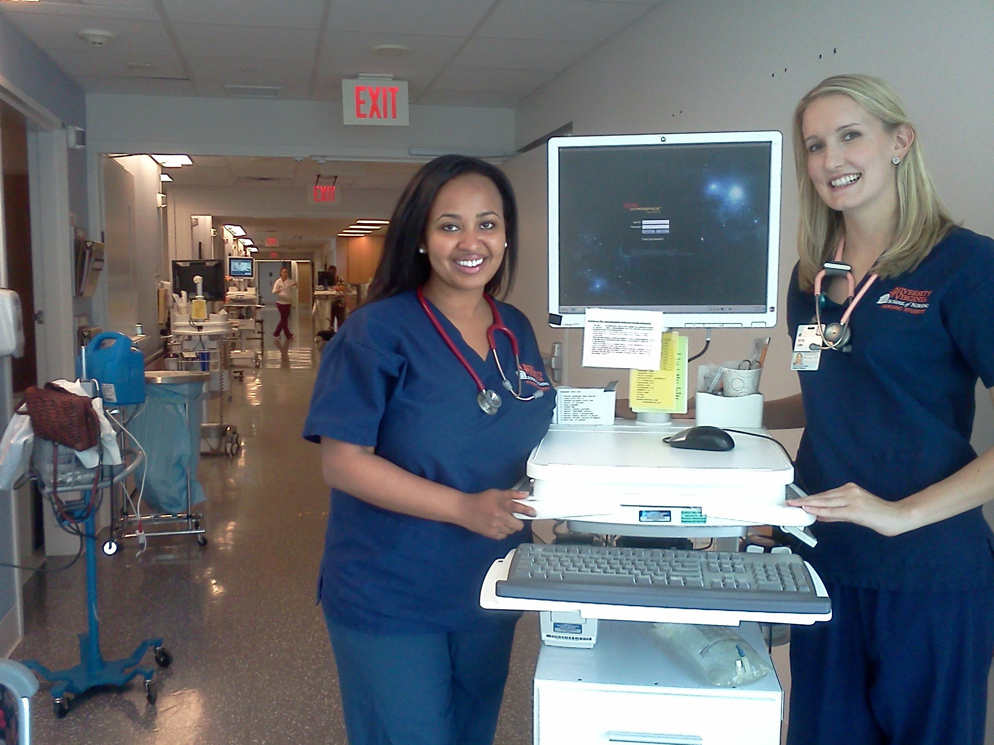 Blen Afework and Amy Lee stand next to a computer cart in the hospital smiling at the camera