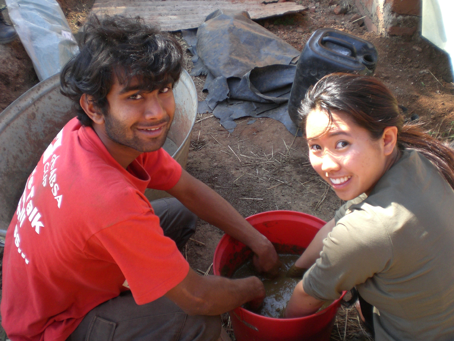 Engineering students with their hands in a five gallon bucket full of mud smiling at the camera