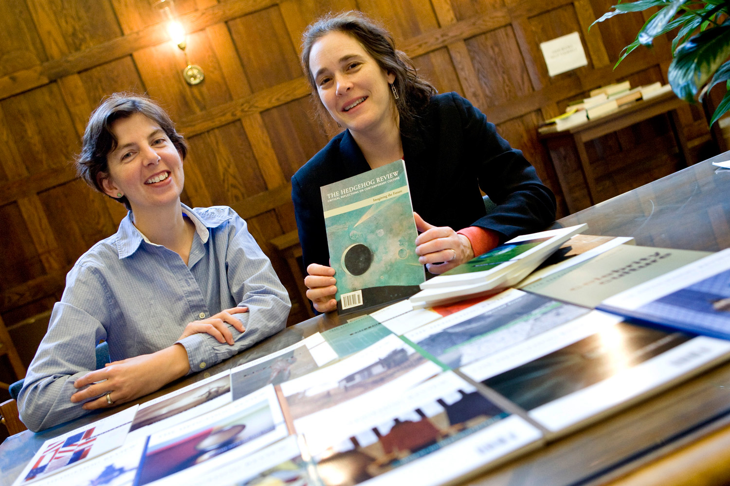Kristine Harmon and Jennifer Geddes sit at a table together with books covering the table