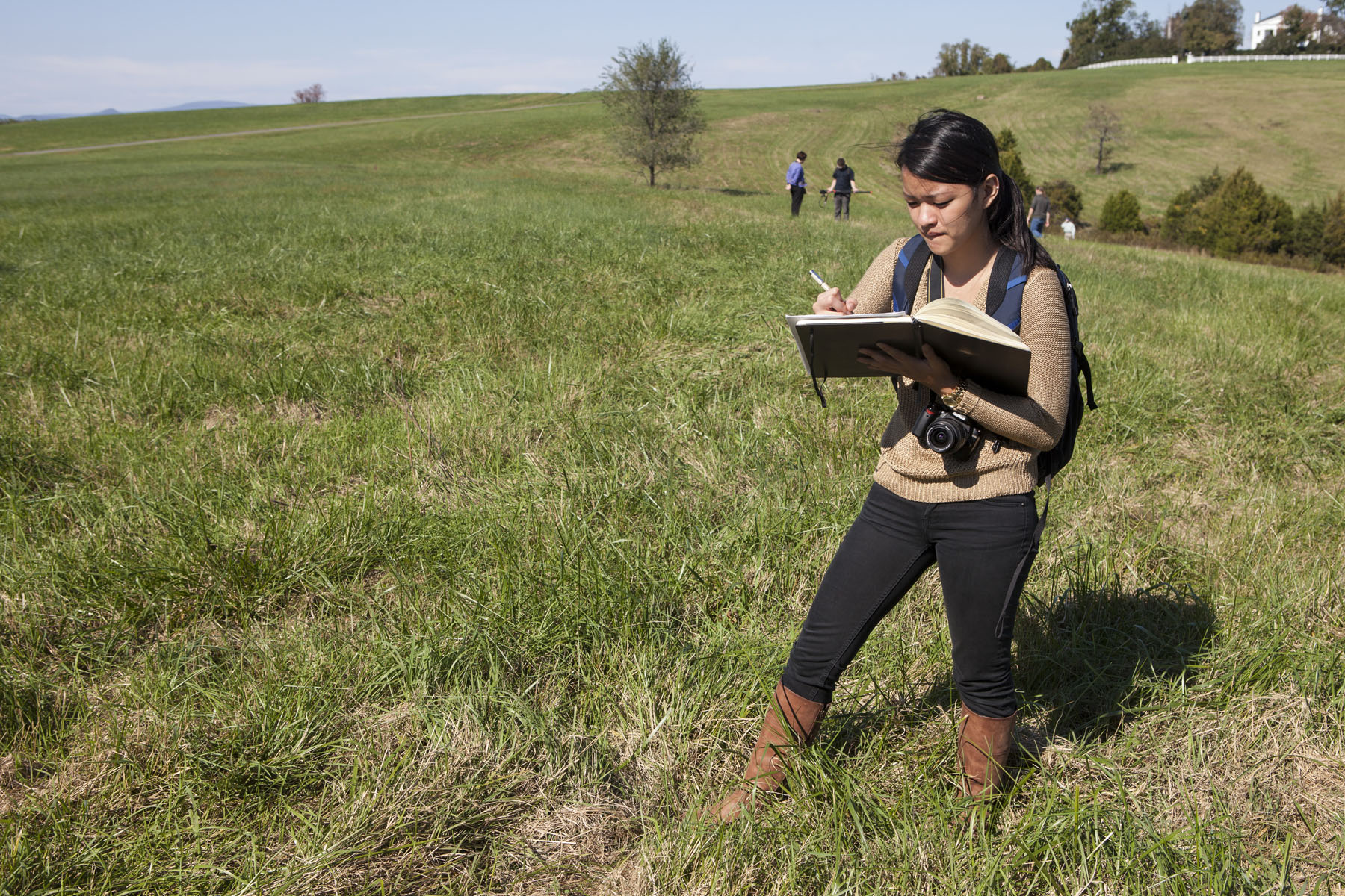 Student standing in a field drawing in a notebook
