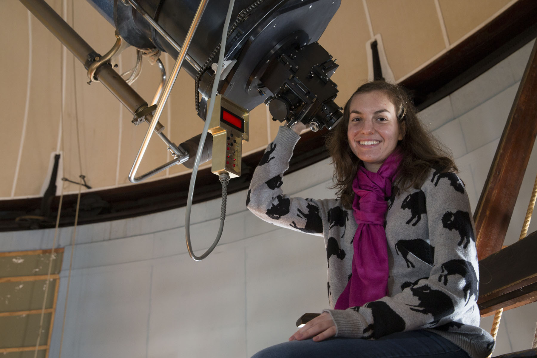 Catherine Zucker sits at the base of a large telescope smiling at the camera