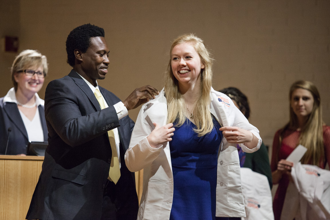 Professor Randy Jones helps a student don a white coat 