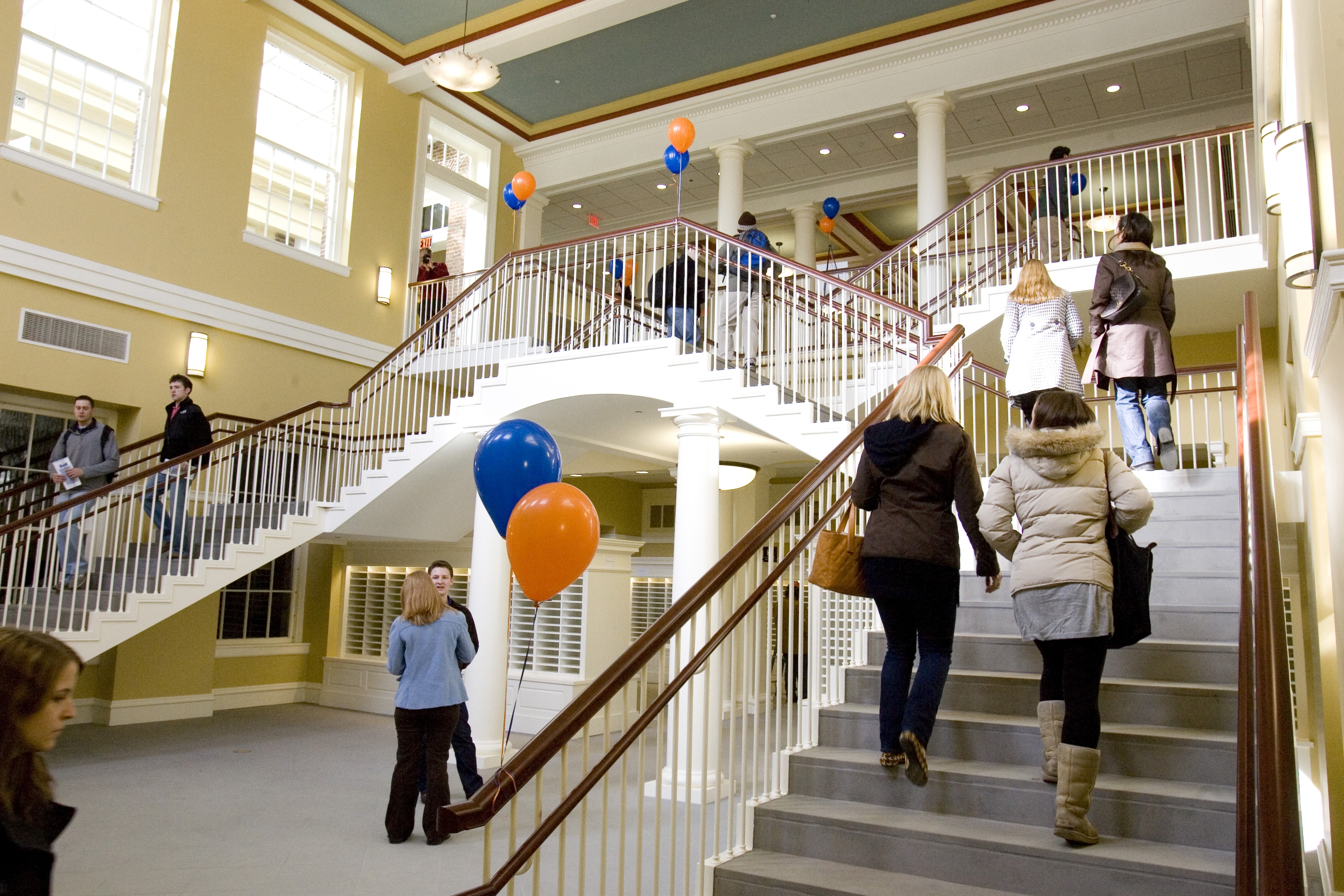people walking up and down a stair case with orange and blue balloons tied on the railings
