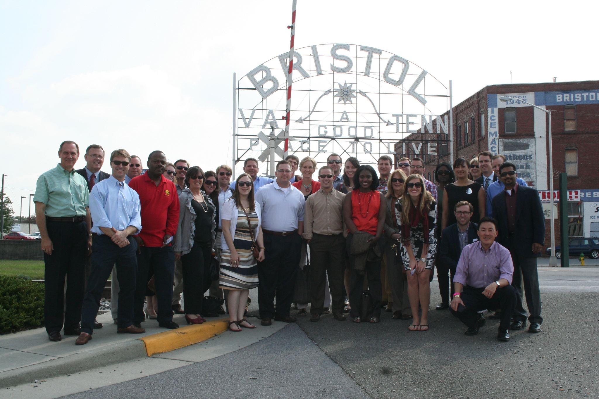 Group photo in front of a sign that says Bristol  va (arrow points right) Tenn (arrow points left)