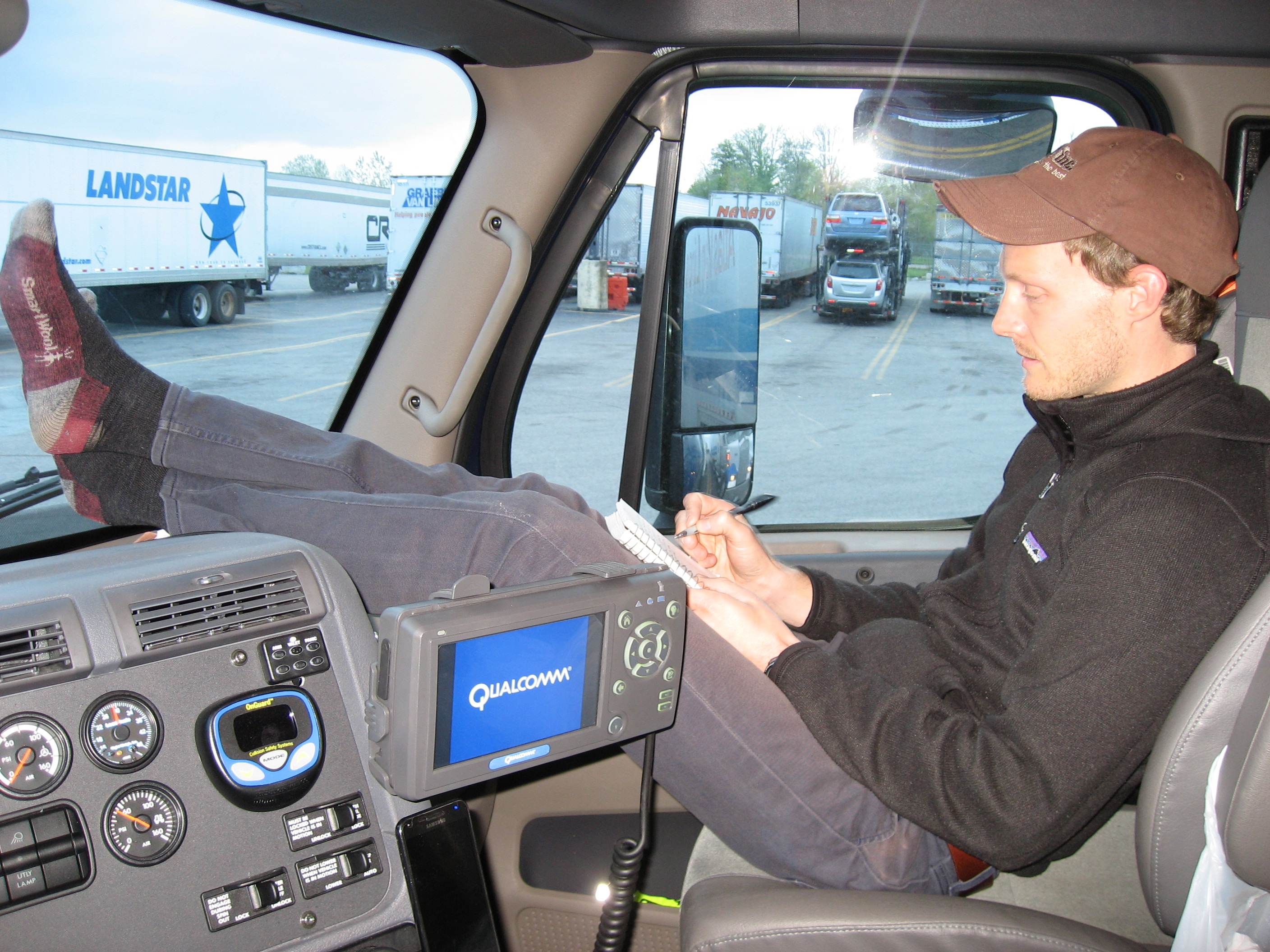 Man sitting in a tractor trailer cab with his feet up writing in a small notebook