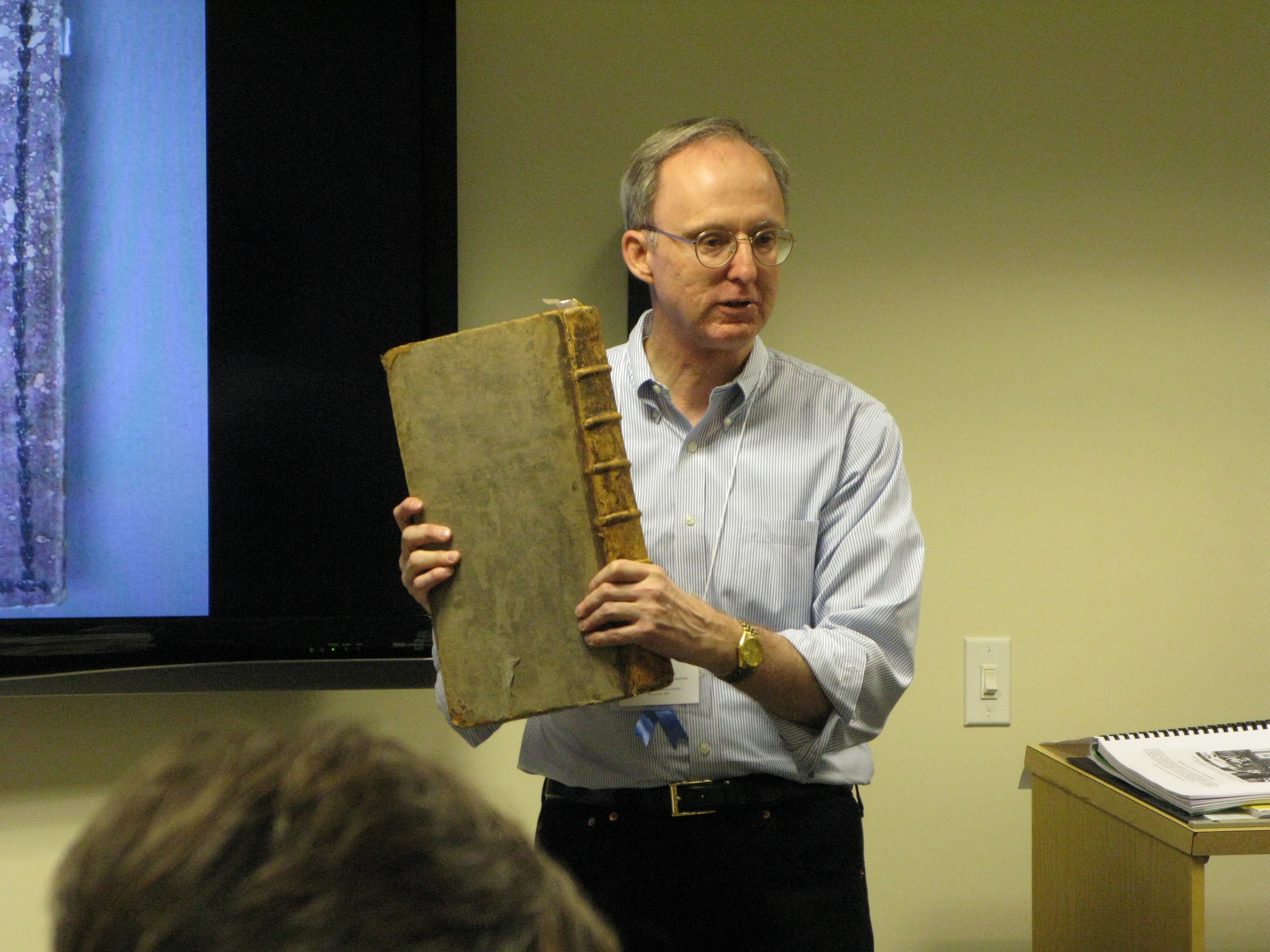 David Whitesell holding a big old book while talking to a group of people