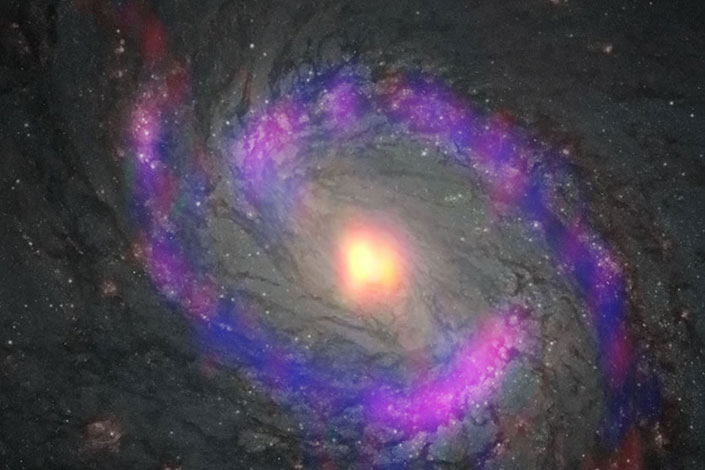 The central part of galaxy M77 is a spiral shape with light and dark purples, grey, and center that is yellow, red, and orange