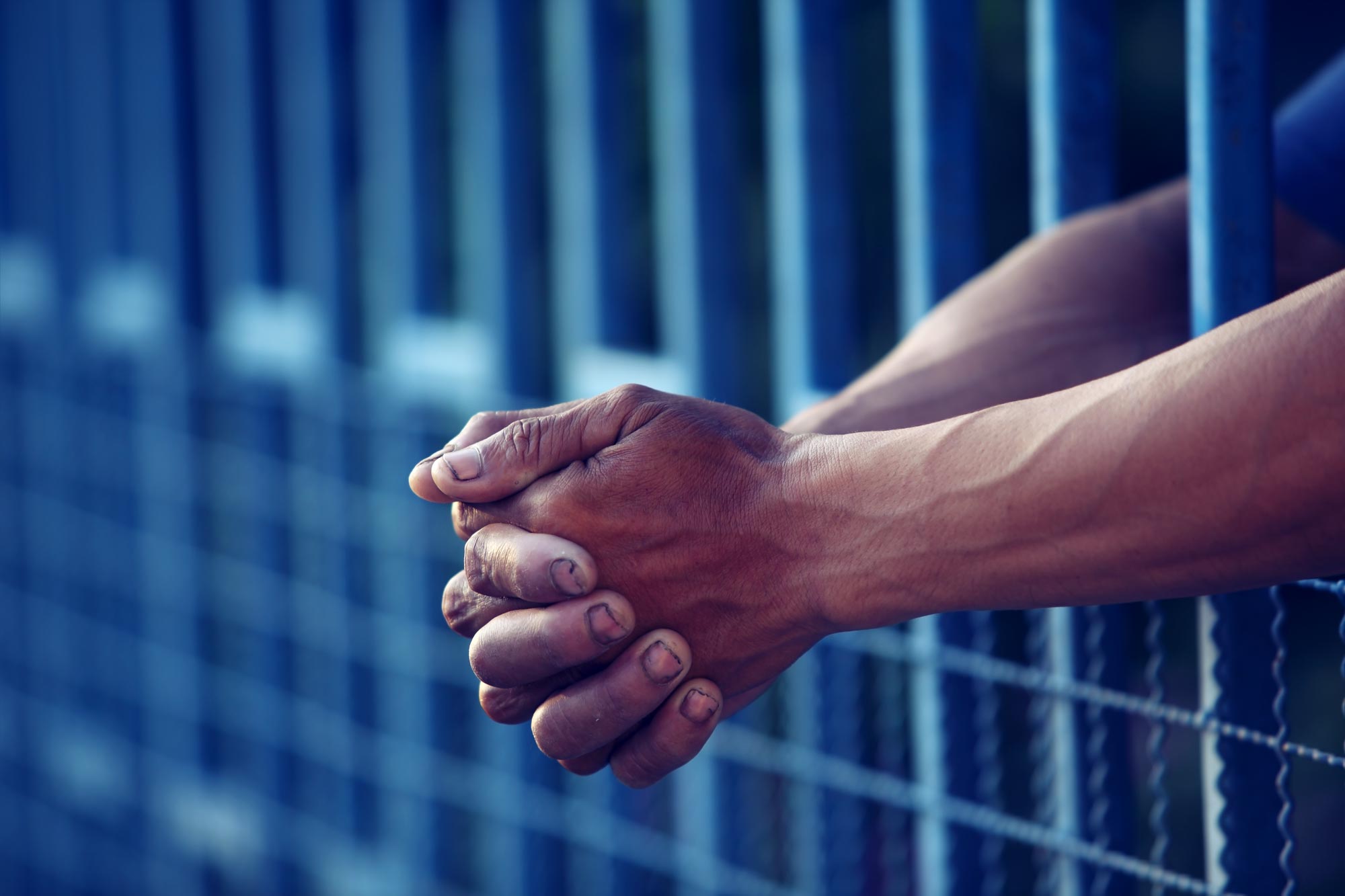 Person with their arms between prison bars hold their own hands
