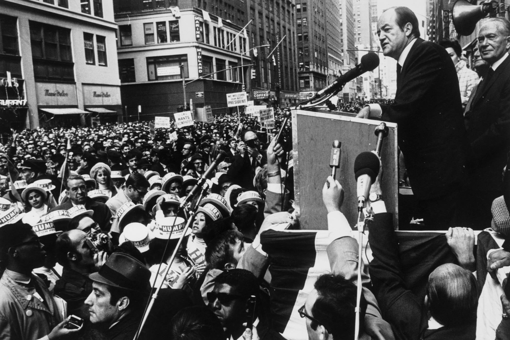 Democrat Hubert H. Humphrey speaking at a podium in New York City to a crowd gathered in the streets during his 1968 presidential campaign.