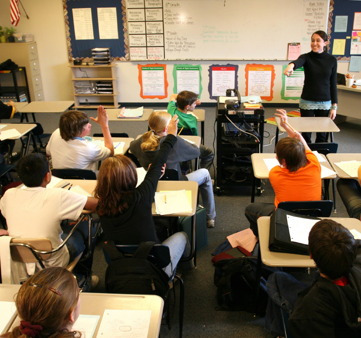 Middle school students raising their hands in a classroom