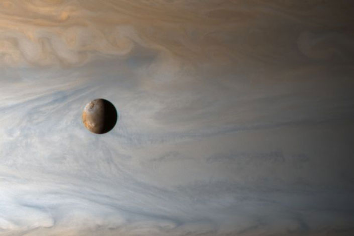 Io over a blue and grey colored Jupiter