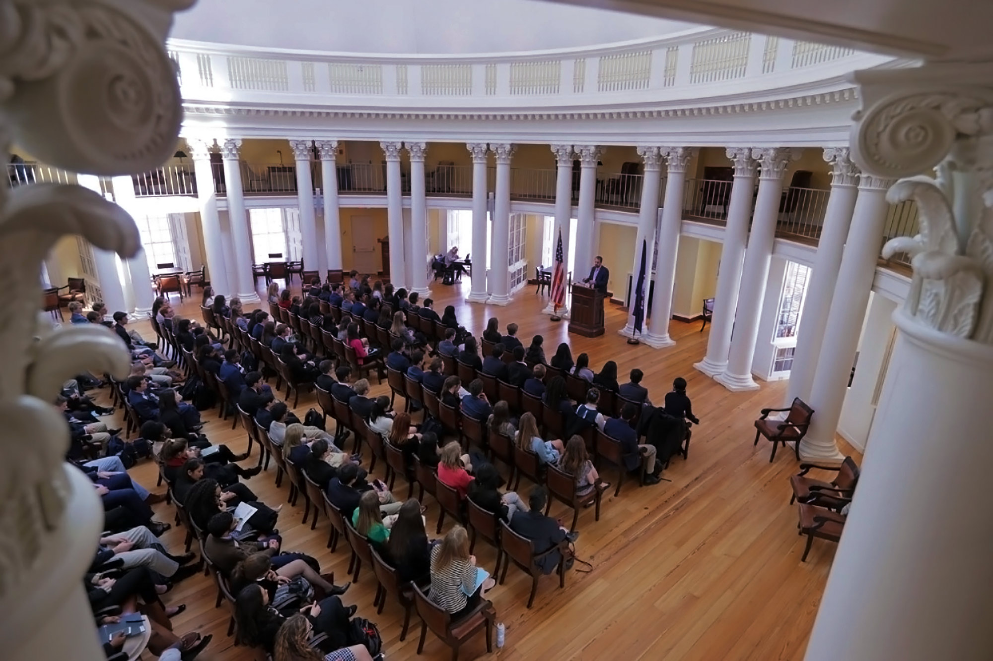 People seating in chairs in the Rotunda's dome room listening to a speaker talking from a podium