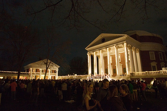 The Rotunda lit up by lights while a choir stands on its steps signing to a crowd on the lawn