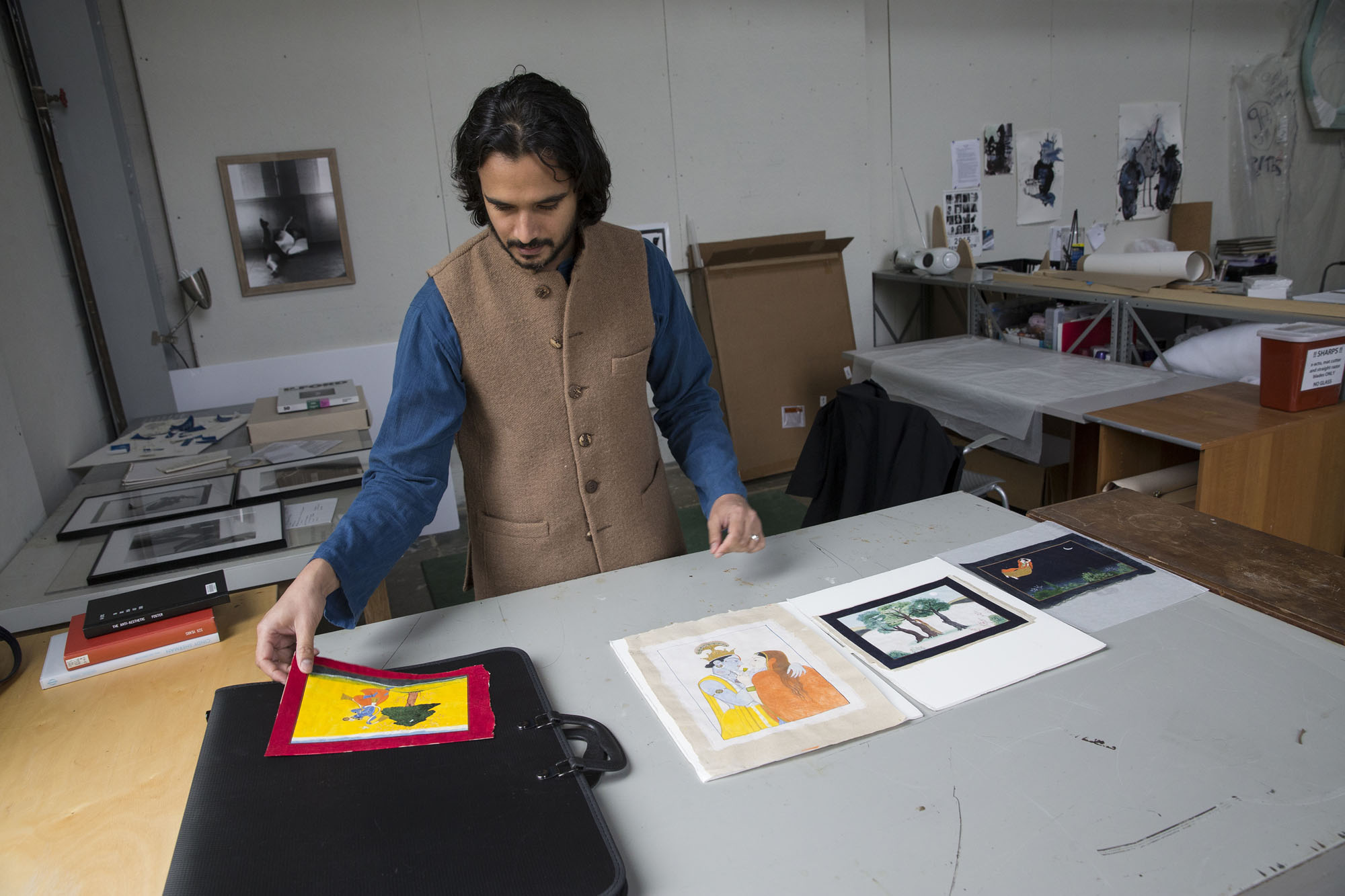Murad Mumtaz laying out paintings he created on a table