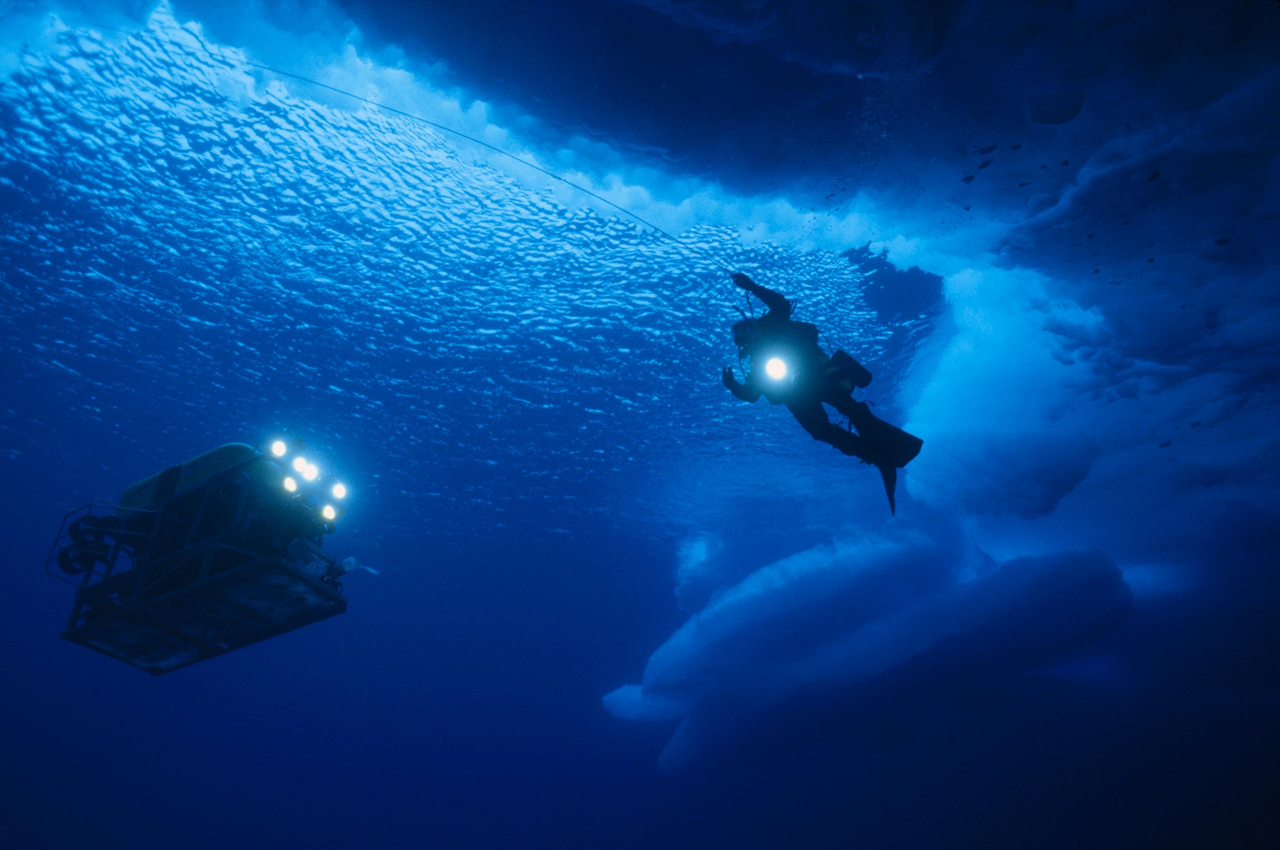 Diver with light in water near icebergs and a lights vehicle is near by
