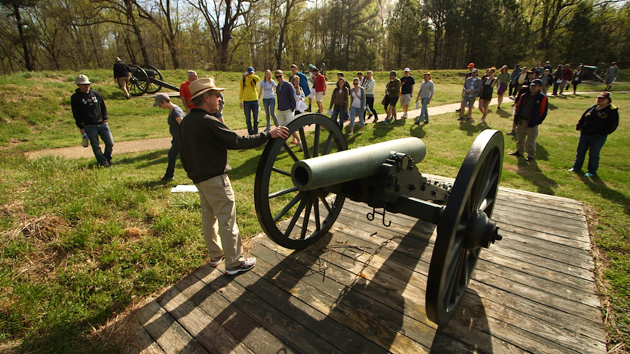 Group of people stand around a tour guide at an old cannon