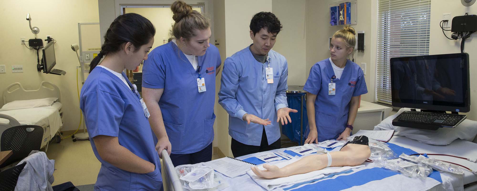 Nursing students listen to an RN talk about a procedure in a simulation lab