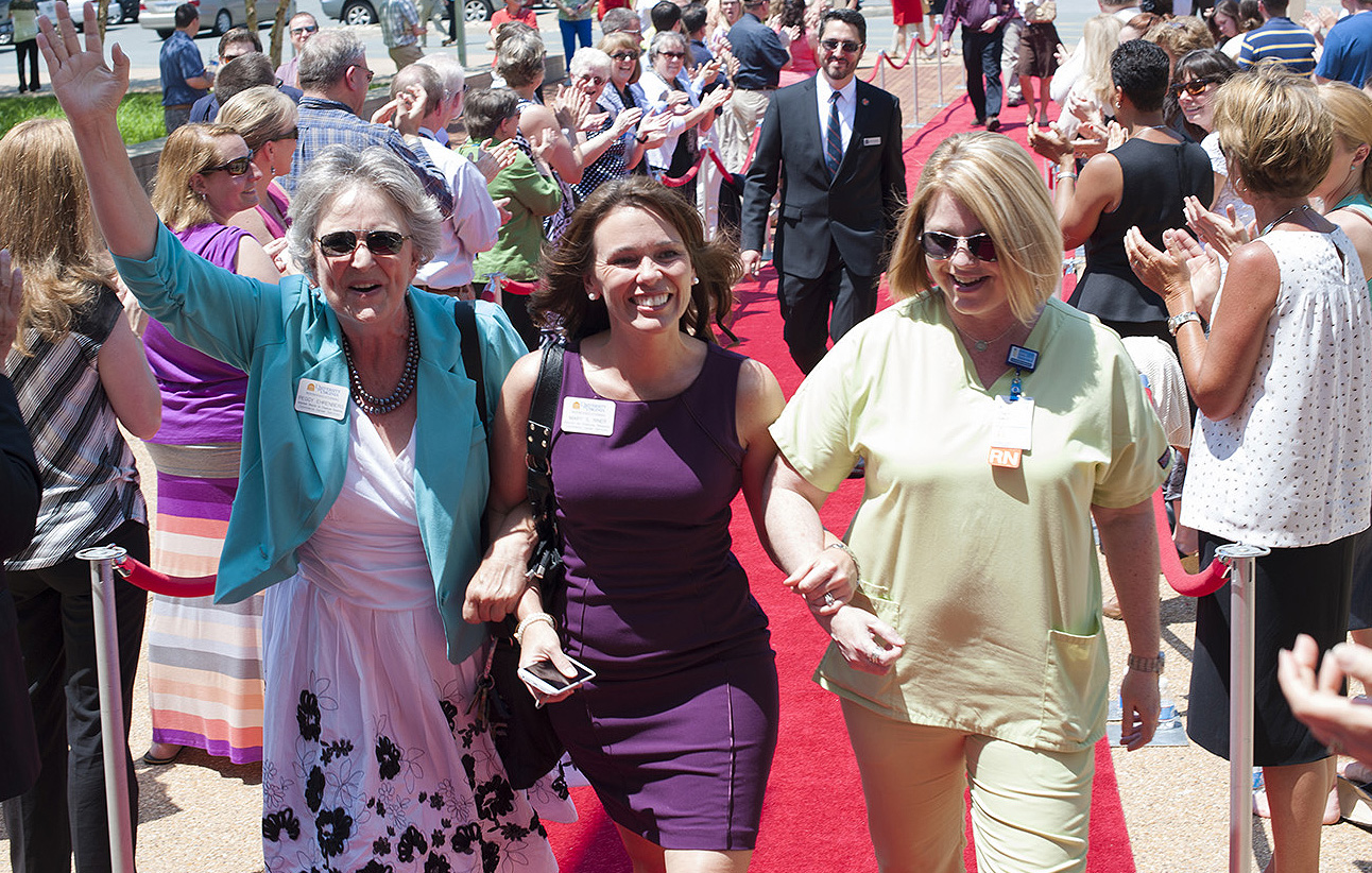 Three women walk arm in arm down a red carpet