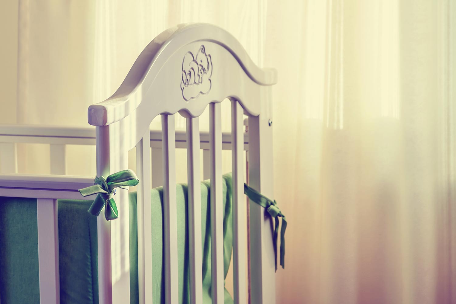 Baby crib with green ribbon holding up the inner pad