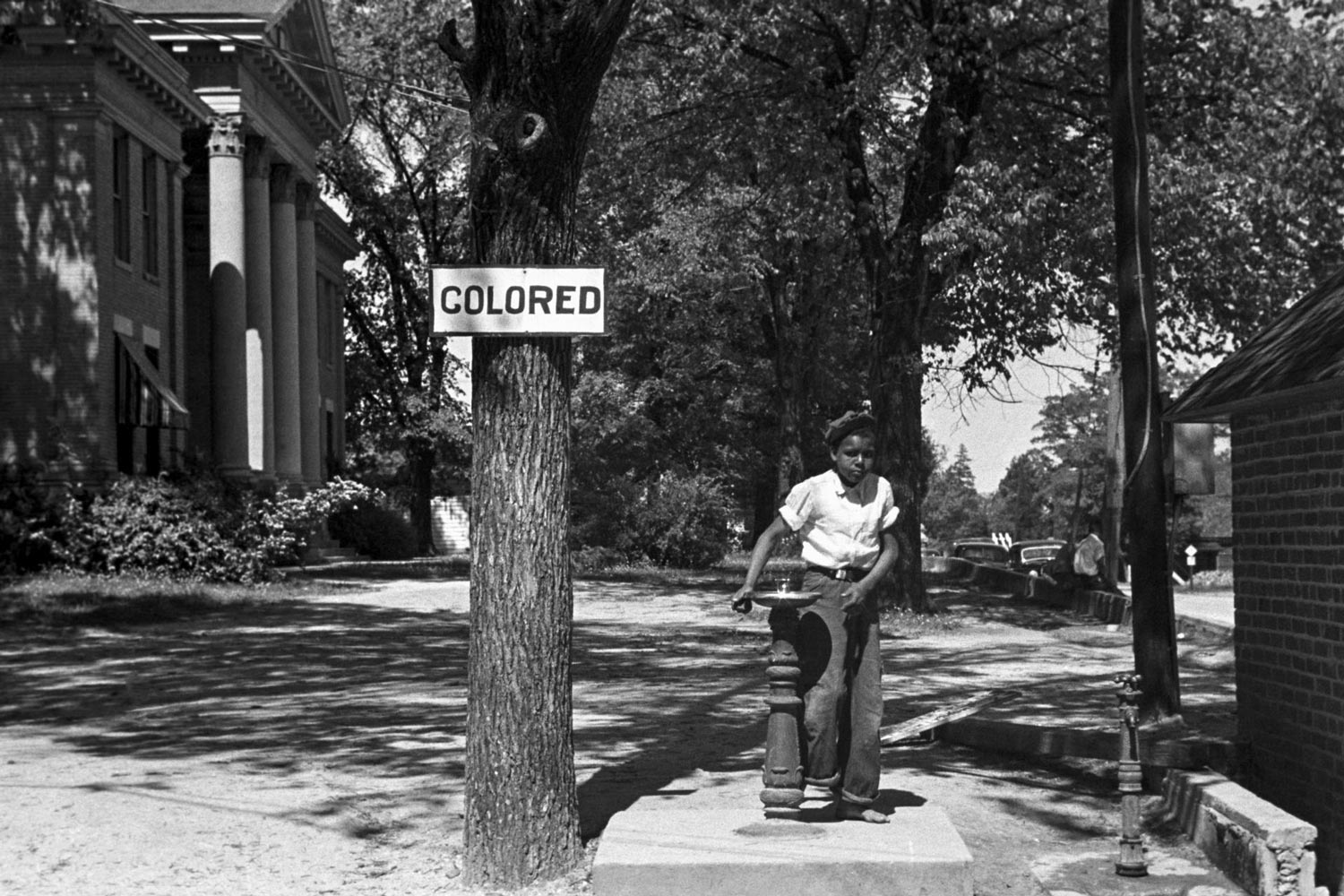 African American boy drinking from a water fountain labeled Colored