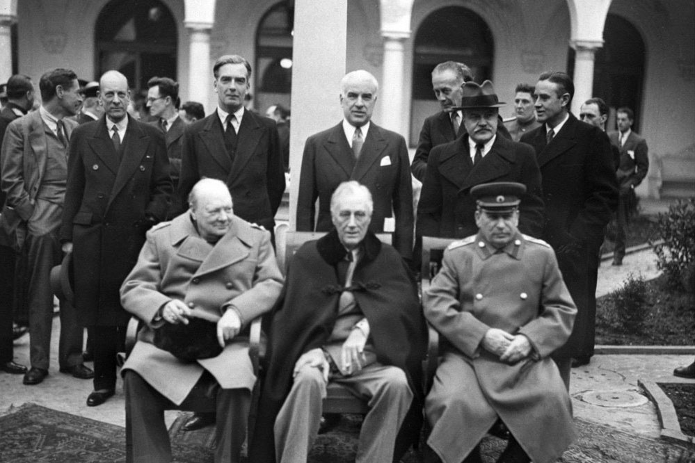 Secretary of State Edward R. Stettinius Jr. stands at center behind (from left) Winston Churchill, Franklin D. Roosevelt and Josef Stalin at the Yalta Conference. Black and white image