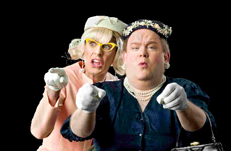 Two actors dressed as women driving a car on stage