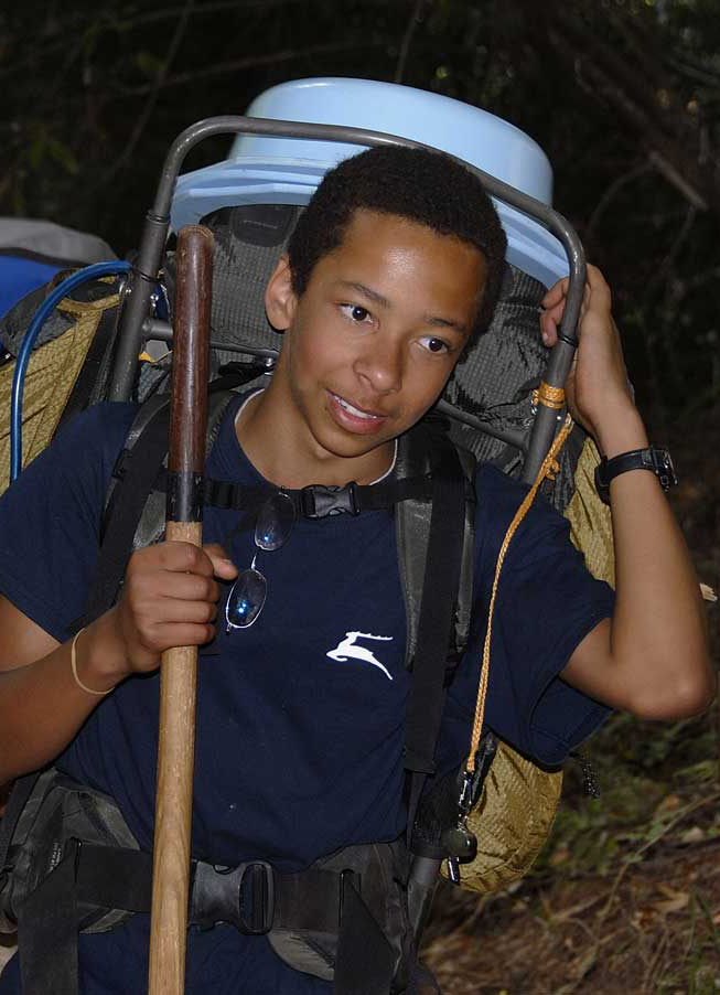 boy carrying a hiking pack and walking stick