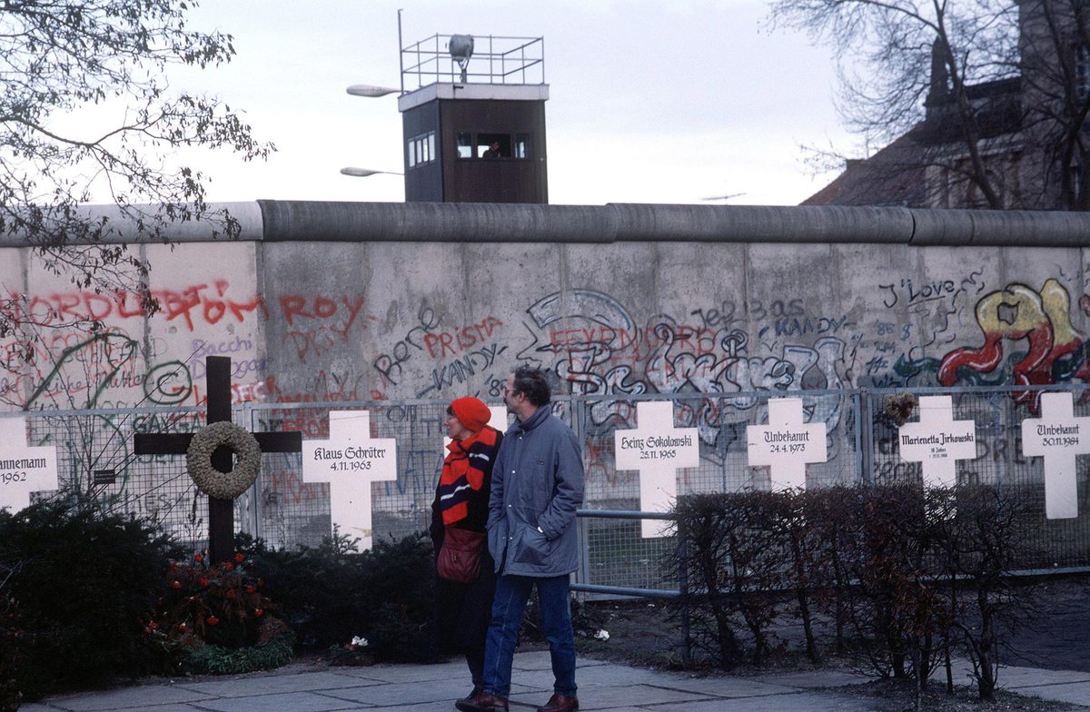 couple walking past crosses lining the Berlin wall