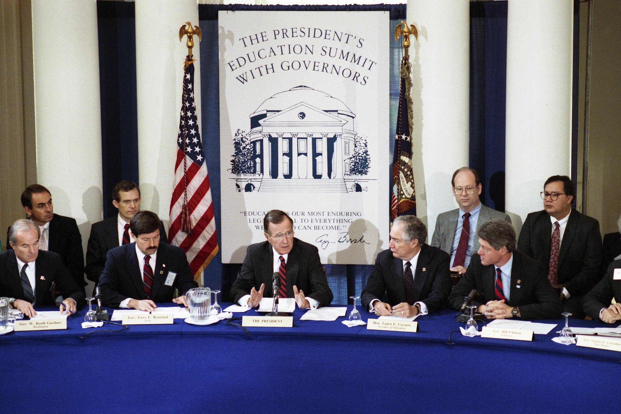Clinton, right, and  President George H.W. Bush, center, sit at a panelist table on a stage