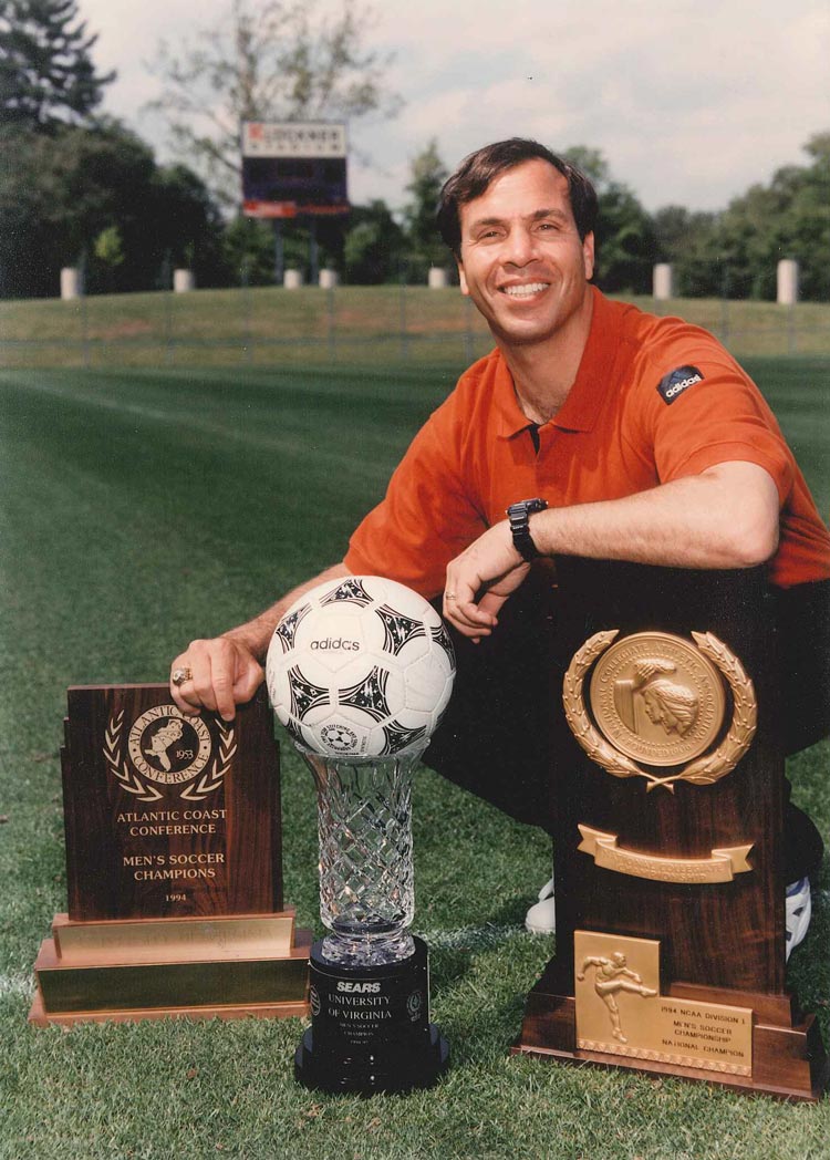 Bruce Arena Bruce Arena bends over to take a picture with the NCAA trophy, and Sears cup trophy