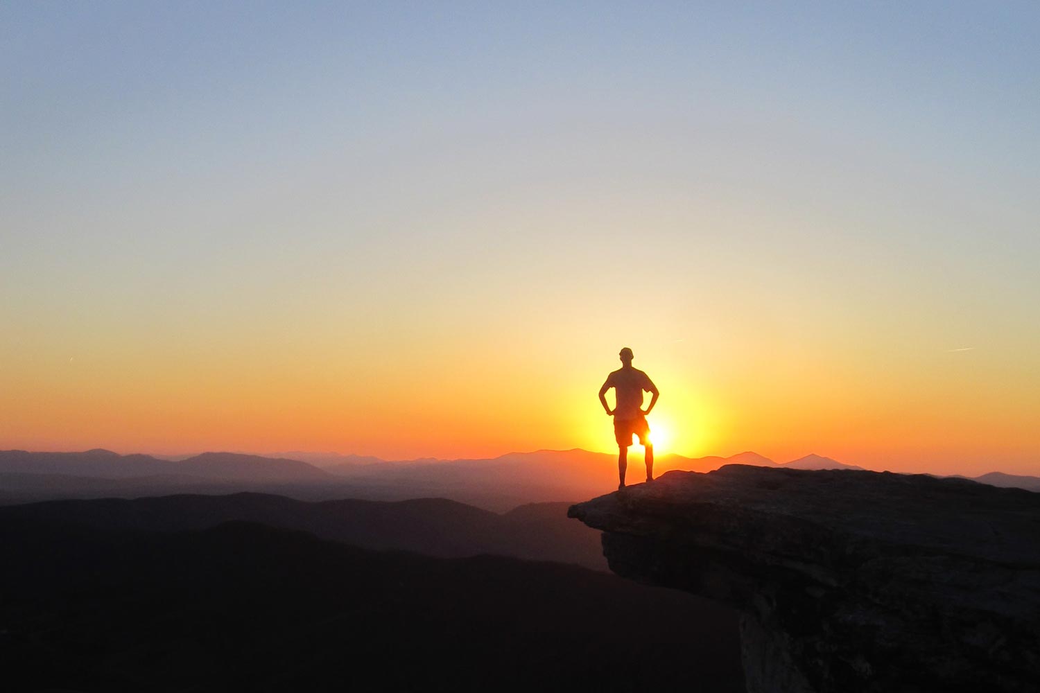 Silhouette of a man standing on a rock ledge during sunset
