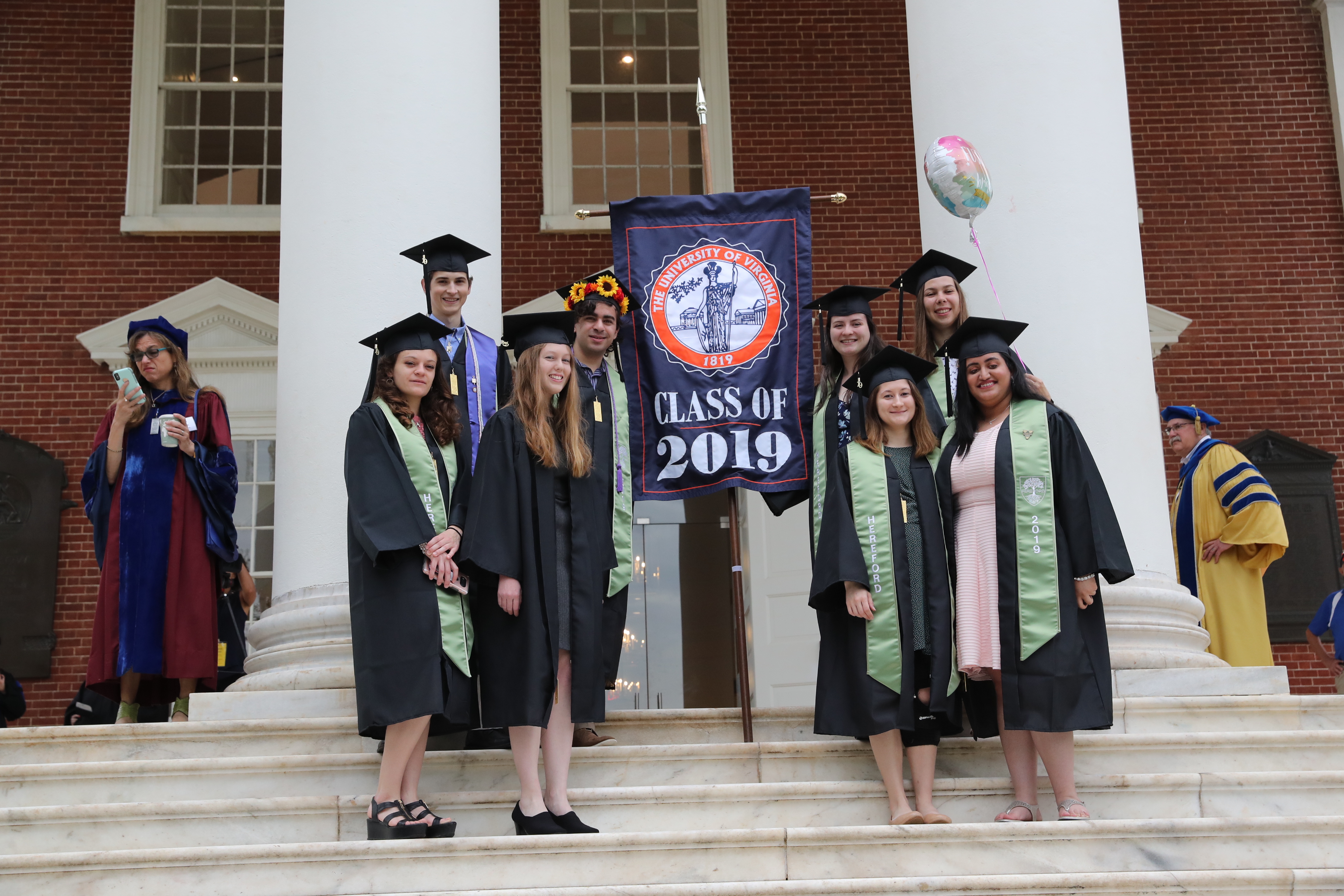 Graduates stand for a group photo next to a banner that says Class of 2019