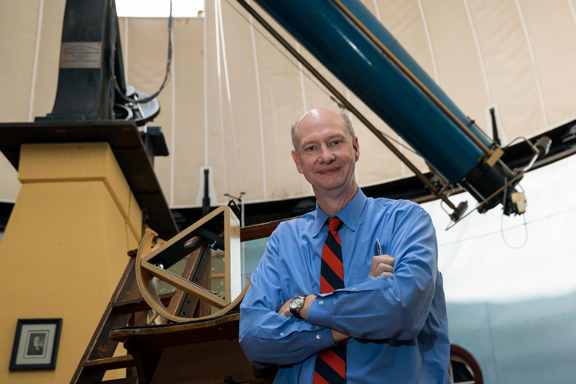 Ed Murphy  standing under a telescope with his arms crossed looking at the camera