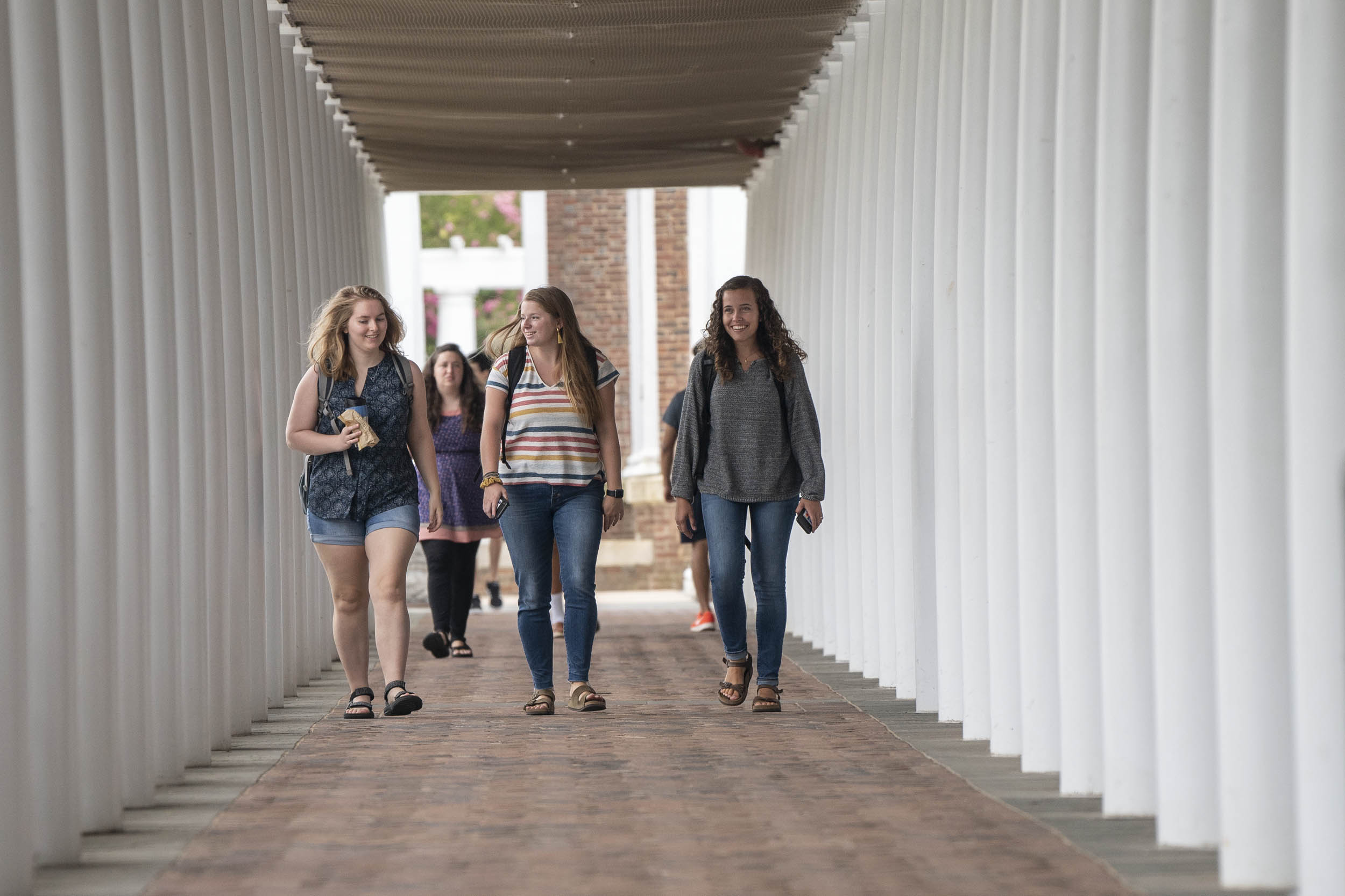 Students walking down a sidewalk lined with white columns