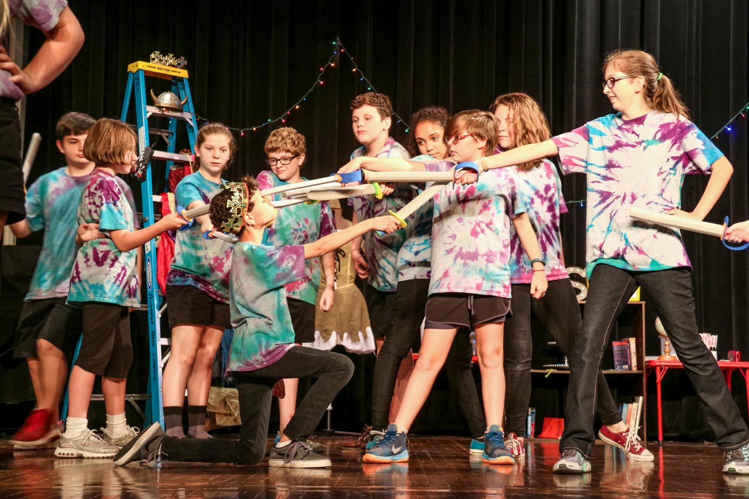 Children point fake swords at another student who is in the middle during a theater camp